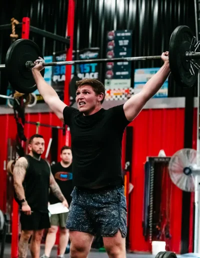 FNL-476 Fit man lifts weights over his head duirng CrossFit DHF training.