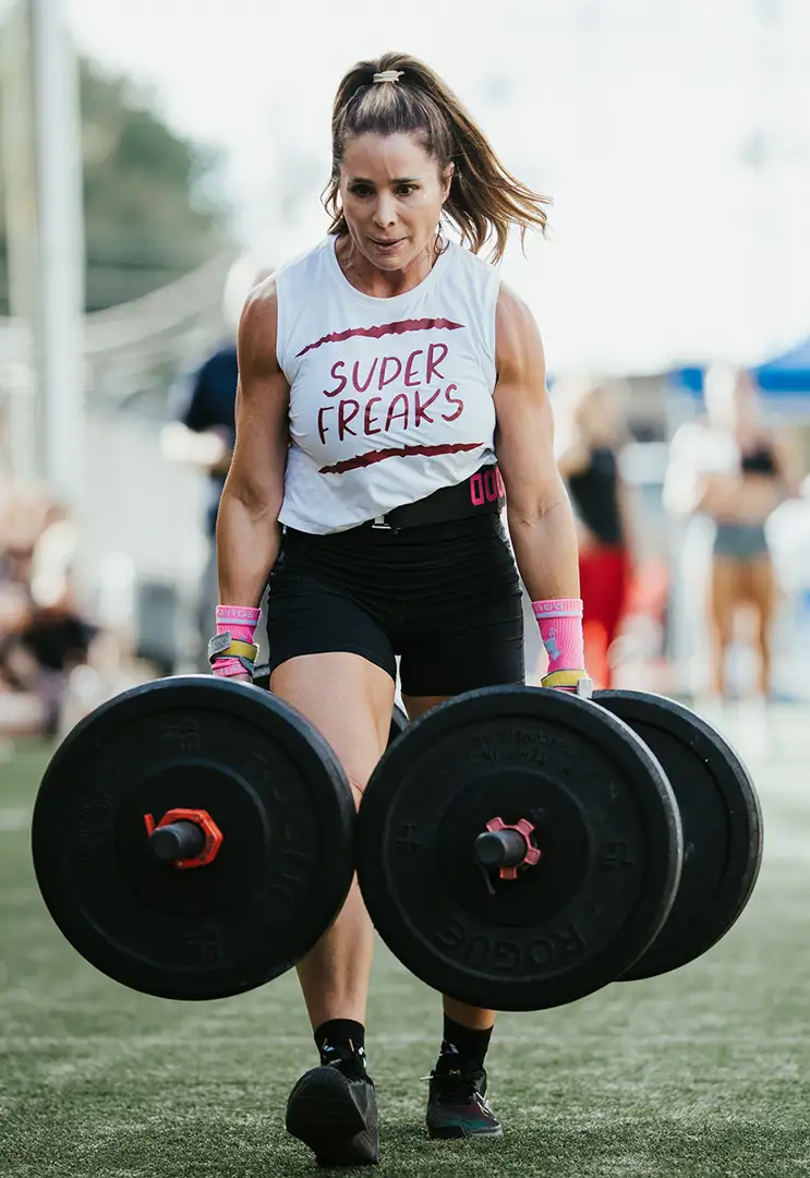 A fit young woman walking while carrying heavy weights during a Fit Fest competition.